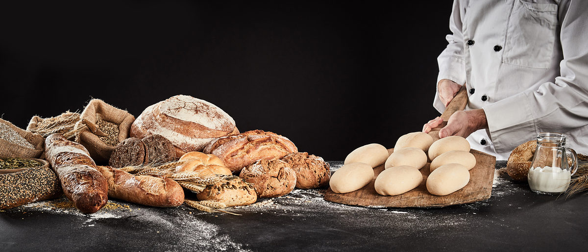 Baker holding a wooden paddle with formed dough ready to bake loaves of speciality bread displayed alongside in banner format Schlagwort(e): accompaniment, baker, bakery, baking, bread, food, gourmet, loaf, preparation, production, roll, speciality, carbohydrate, cereal, wheat, grain, chef, dough, holding, paddle, raw, ready, wooden, bagels, display, prepare, preparing, copy space, copy-space, copyspace, advertising, craft, bake, bakehouse, bakers, shop, whole, wholegrain, wholemeal, background, black, dark, banner, header, panorama, accompaniment, baker, bakery, baking, bread, food, gourmet, loaf, preparation, production, roll, speciality, carbohydrate, cereal, wheat, grain, chef, dough, holding, paddle, raw, ready, wooden, bagels, display, prepare, preparing, copy space, copy-space, copyspace, advertising, craft, bake, bakehouse, bakers, shop, whole, wholegrain, wholemeal, background, black, dark, banner, header, panorama