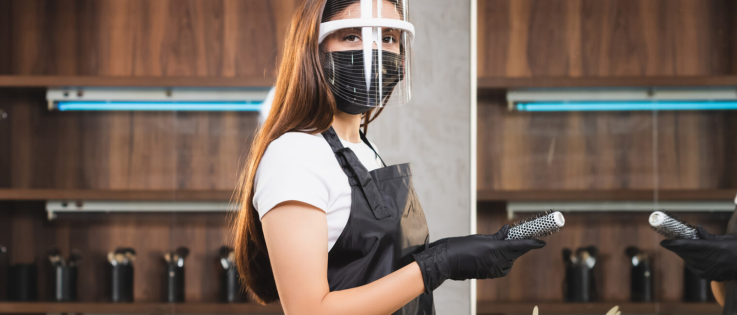 young hairdresser in face shield and latex gloves holding comb while looking at camera, banner Schlagwort(e): horizontal,equipment,young,adult,beauty,caucasian,medicine,healt, horizontal, equipment, young, adult, beauty, caucasian, medicine, healthcare, crop, banner, personal, service, woman, professional, work, tool, comb, salon, protective, indoors, safety, hairdresser, uniform, virus, workplace, workwear, barber, barbershop, corona, epidemic, pandemic, infection, apron, ppe, quarantine, hairstylist, looking at camera, copy space, one person, medical mask, latex gloves, face shield, coronavirus, website header, 2019-ncov, covid-19