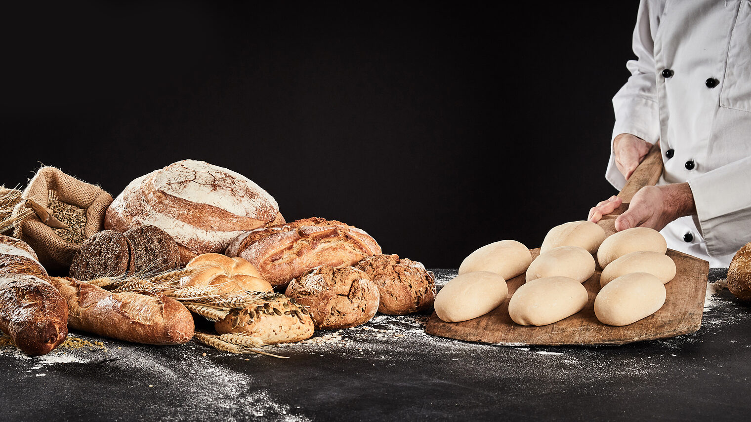 Baker holding a wooden paddle with formed dough ready to bake loaves of speciality bread displayed alongside in banner format Schlagwort(e): accompaniment, baker, bakery, baking, bread, food, gourmet, loaf, preparation, production, roll, speciality, carbohydrate, cereal, wheat, grain, chef, dough, holding, paddle, raw, ready, wooden, bagels, display, prepare, preparing, copy space, copy-space, copyspace, advertising, craft, bake, bakehouse, bakers, shop, whole, wholegrain, wholemeal, background, black, dark, banner, header, panorama, accompaniment, baker, bakery, baking, bread, food, gourmet, loaf, preparation, production, roll, speciality, carbohydrate, cereal, wheat, grain, chef, dough, holding, paddle, raw, ready, wooden, bagels, display, prepare, preparing, copy space, copy-space, copyspace, advertising, craft, bake, bakehouse, bakers, shop, whole, wholegrain, wholemeal, background, black, dark, banner, header, panorama