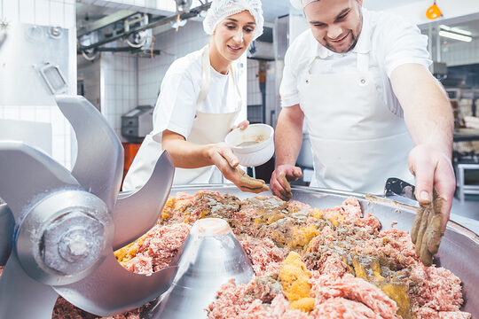 Butchers putting spices in minced meat to make sausages Schlagwort(e): Butcher, butchery, man, woman, team, Production, making, Meat, raw, minced, grounded, pork, beef, Machine, mixer, cutter, blender, grinder, chopper, mincer, meat grinder, occupation, working, work, worker, Cutting, processing, spices, spice, Business, food, fresh, men at work, food industry, industry, traditional, People, person, Caucasian, uniform, male, female, Germany, German, metzger, fleischer, gehacktes, hack, hackfleisch, schlachter, metzgerei, fleischerei, mann, frau, team, herstellung, machen, herstellen, wursten, fleisch, rohmasse, wurst-rohmasse, rind, schwein, schweinefleisch, rindfleisch, roh, mett, maschine, fleischwolf, kutter, mischer, beruf, arbeit, arbeiten, handwerk, meister, geselle, verarbeitung, verarbeiten, würzen, gewürze, lebensmittelindustrie, frisch, nahrungsmittel, essen, ernährung, produktion, traditionell, menschen, leute, arbeiter, deutschland, deutsch