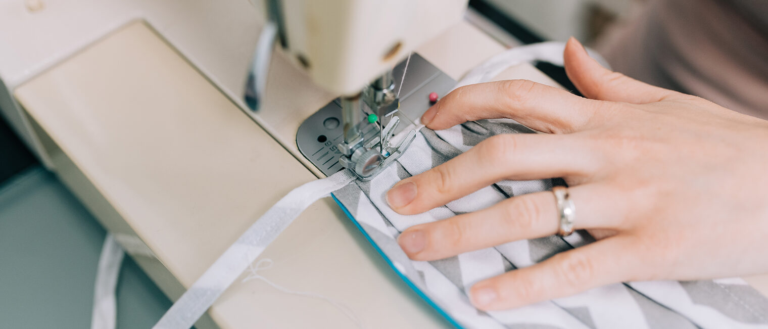 Woman hands using the sewing machine to sew the face medical mask during the coronavirus pandemia. Home made diy protective mask against virus. Schlagwort(e): corona virus, medical material, handmade, respiratory, covid19, corona-virus, infection, handicraft, clothing, person, equipment, seamstress, covid, 2019-ncov, filter, health, closeup, fabric, detail, cloth, needle, face, covid-19, coronavirus, sew, mask, sewing, design, pattern, sewing machine, face mask, shortage, cotton, medical, fashion, machine, material, spread, clothes, thread, process, stitch, human hand, hand, seam, industry, combat, tailor, needlework, woman